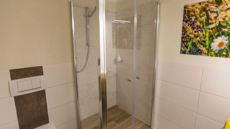 Ein modernes Badezimmer mit einer Dusche aus Glas und hellen Fliesen. An der Wand hängt ein Bild von Blumen.