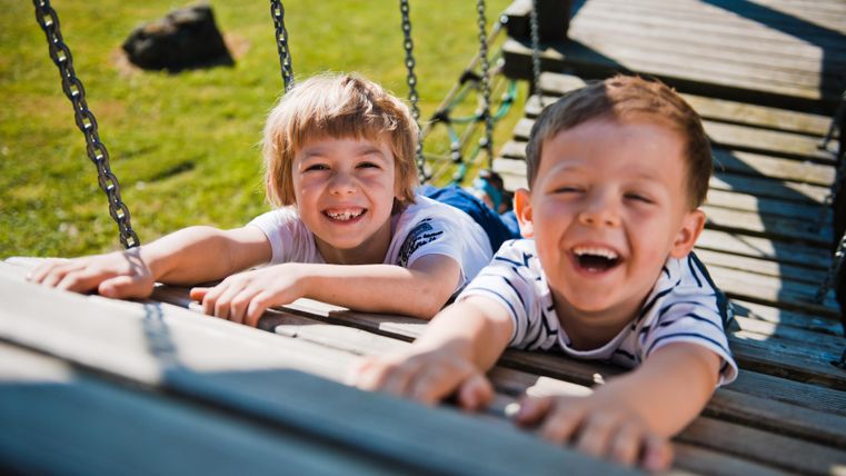 Twee lachende kinderen liggen op een schommel en hebben plezier. Ze genieten van een zonnige dag buiten.