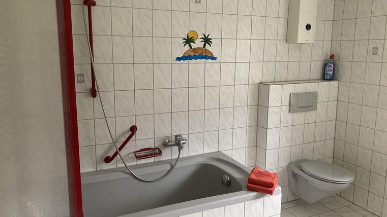 Een moderne badkamer met een bad en een douche. De muren zijn betegeld en er is een toiletruimte.