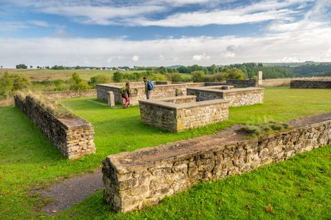 Ruïnes van een oud complex op een groene weide met uitzicht op de omgeving. Twee personen verkennen de historische stenen.