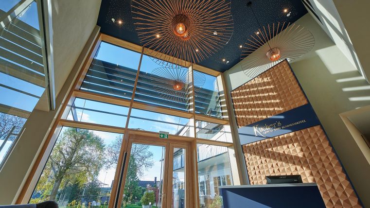 Ein modernes Foyer mit großen Fenstern und einem stilvollen Deckenleuchter. Der Empfangstresen ist in einem eleganten Design gestaltet.