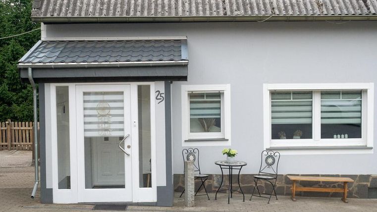 Ein modernes Haus mit grau gestrichener Fassade und einem einladenden Eingangsbereich. Draußen steht ein kleiner Tisch mit Stühlen und einer Blumendekoration.