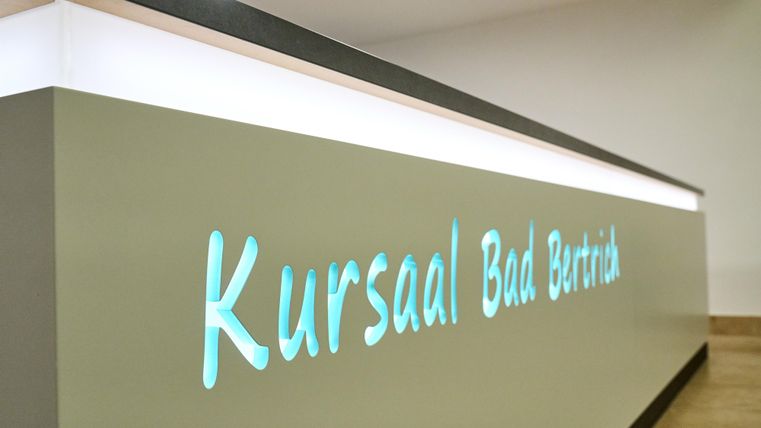 Ein moderner Empfangstresen mit der Aufschrift "Kursaal Bad Bertrich". Die Beleuchtung sorgt für eine einladende Atmosphäre.