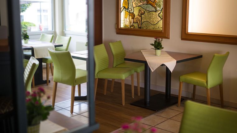 Ein gemütliches Restaurant mit grünen Stühlen und Holzdekor. Die Tische sind ordentlich mit Tischdecken und Pflanzen dekoriert.