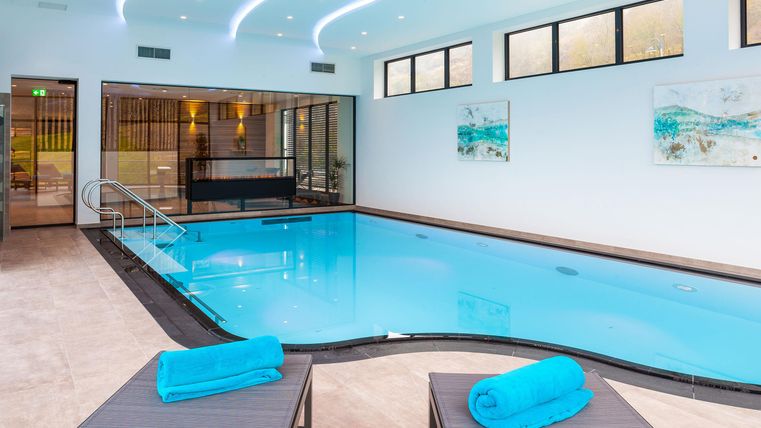 Ein stilvoller Innenpool mit klaren Wasser und modernen Liegen. Helle Wände und große Fenster sorgen für eine angenehme Atmosphäre.