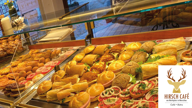 A selection of delicious baked goods and snacks in a glass showcase. In the background, fresh rolls and various sandwiches can be seen.