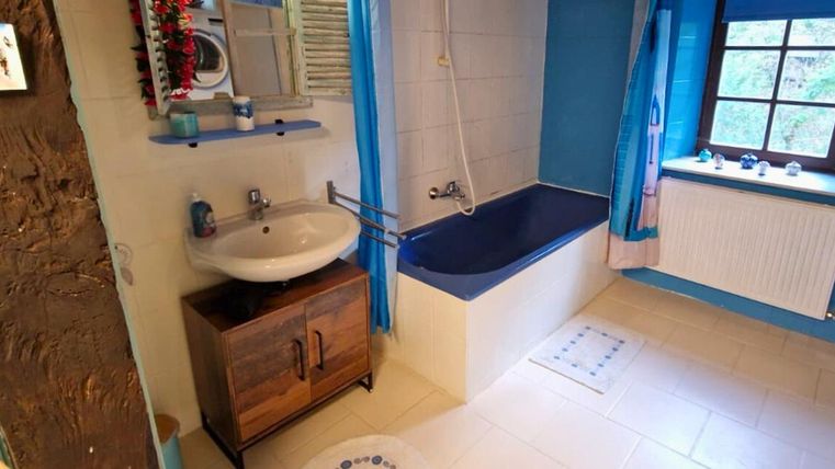 A modern bathroom with blue accents and a bathtub. There is a sink, a mirror, and a window with a view.