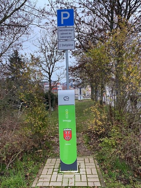 A charging station for electric cars with a space indication. The station is surrounded by trees and shrubs.