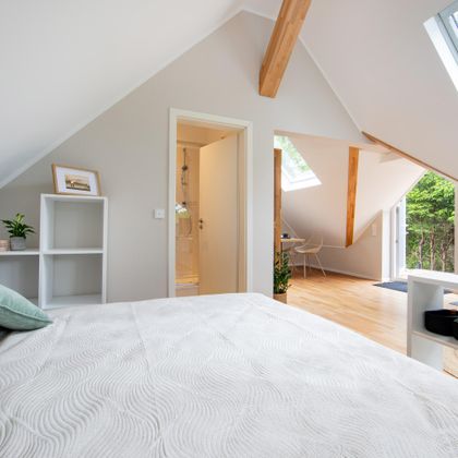 Een moderne slaapkamer met schuine wanden en houten details. Er zijn ramen die veel licht binnenlaten en uitzicht op de buitenlucht bieden.