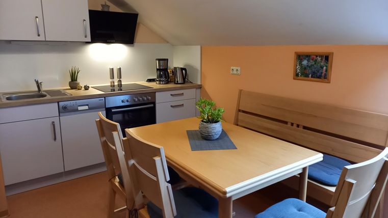 Een gezellige keuken met een eettafel en stoelen. De muren zijn oranje, en er is een moderne keukeninrichting.