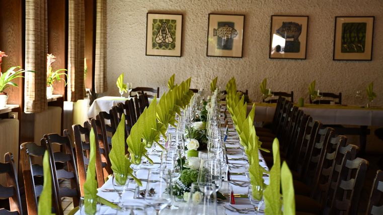 Ein elegant gedeckter Tisch in einem Restaurant. Grünes Besteck und Blumen verleihen dem Raum eine frische Atmosphäre.