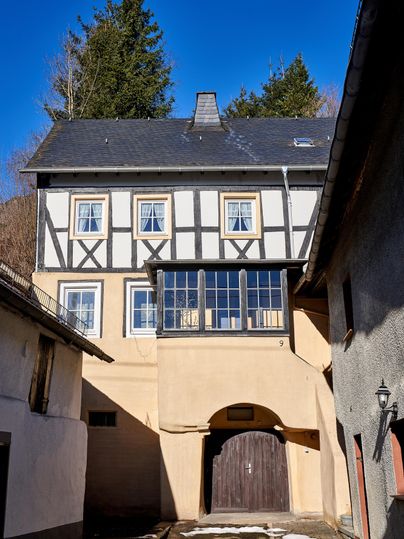 A traditional half-timbered house with a combination of wood and stone cladding. The sky is clear and the surroundings are rural.