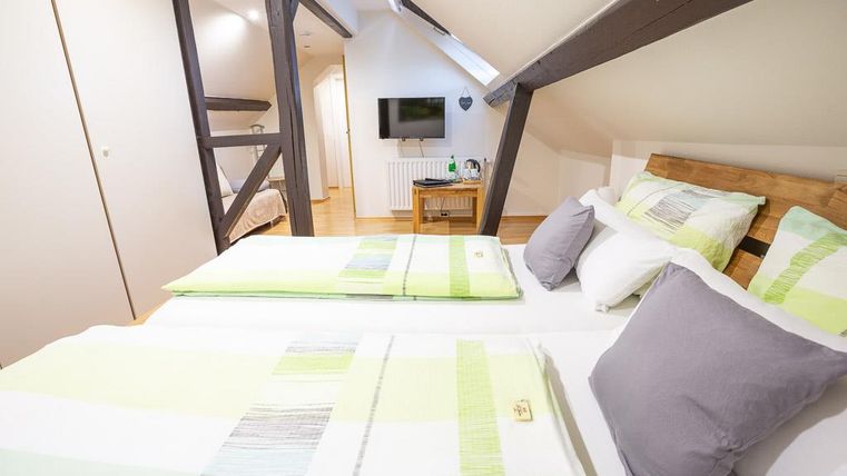 A cozy bedroom with two beds decorated with bright, striped bedding. The wooden ceiling and the television in the background create an inviting atmosphere.