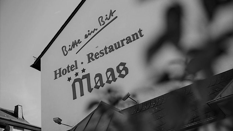 Een kijk op de façade van een hotel en restaurant met de naam „Maas“. De letters zijn opvallend en uitnodigend.