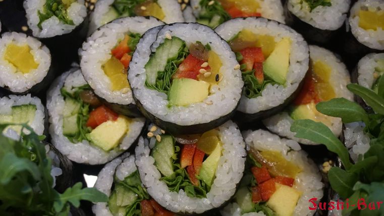 Eine Auswahl von Sushi-Rollen mit verschiedenen Füllungen wie Gemüse und Avocado. Die Rollen sind mit schwarzem Nori und Sesamsamen garniert.