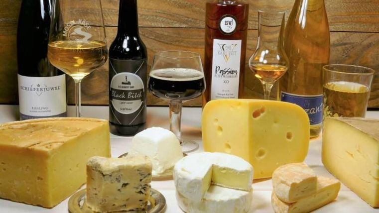 A selection of different types of cheese and drinks on a table. Wooden panels are visible in the background.