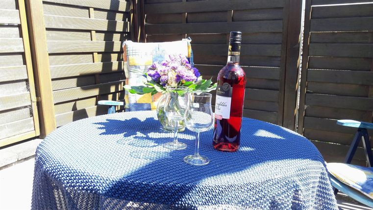 Een mooie tafel buiten met een fles wijn en twee glazen. Een klein vaasje met kleurrijke bloemen staat ook op de tafel.