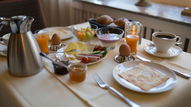 Ein reichhaltiges Frühstücksbuffet mit Kaffee, frischen Brötchen, Eiern und einer Auswahl an Früchten. Auf dem Tisch befinden sich auch Marmelade und verschiedene Käsesorten.
