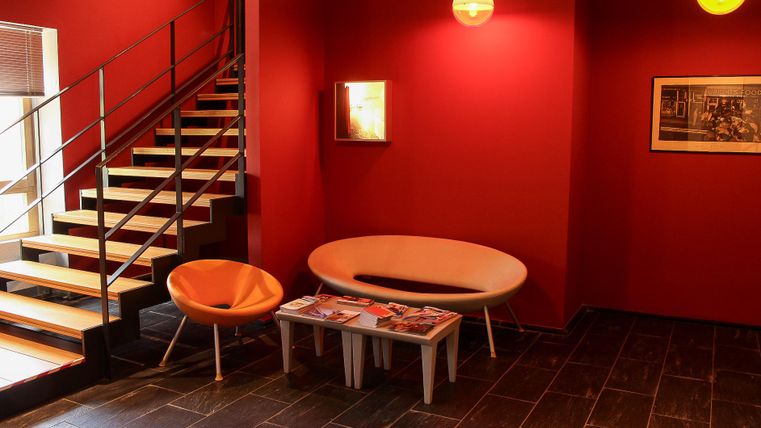 A modern living room with red walls and stylish furniture. The staircase in the background adds an elegant touch to the space.