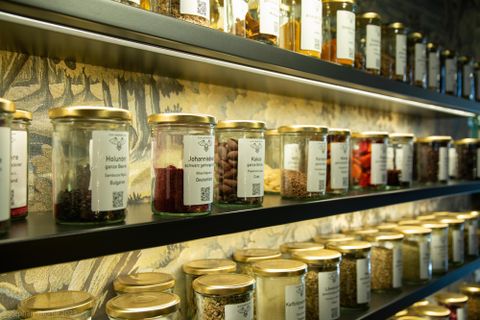 Eine gut sortierte Wand mit Gläsern voller Gewürze und Kräuter. Die Gläser haben etikettierte Beschriftungen und sind in einer ansprechenden Anordnung präsentiert.