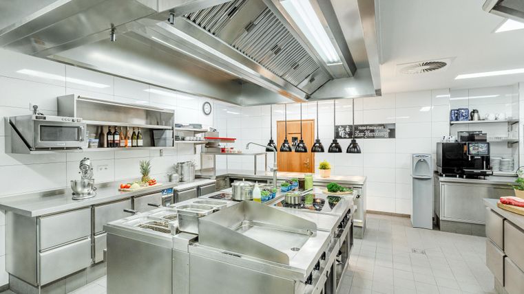 Moderne Restaurantküche mit Edelstahlgeräten und Zutaten auf Arbeitsflächen.