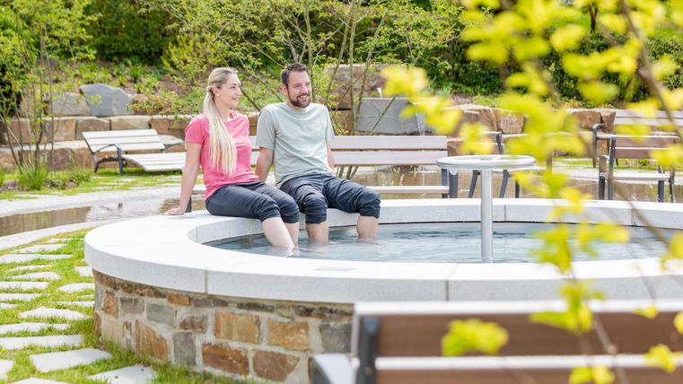 Ein entspannendes Spa mit einem warmen Sprudelbad. Ein Paar sitzt gemütlich am Rand und genießt die meiste Zeit im Freien.