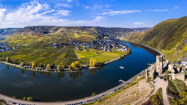 Eine malerische Landschaft mit einem geschwungenen Fluss, umgeben von sanften Hügeln und grünen Wiesen. Der Himmel ist klar und die Sonne scheint hell.