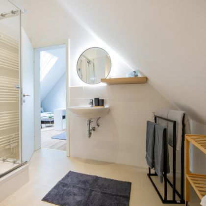 Een moderne badkamer met een douche en een spiegel. Houten planken en handdoeken geven de ruimte een gezellige sfeer.