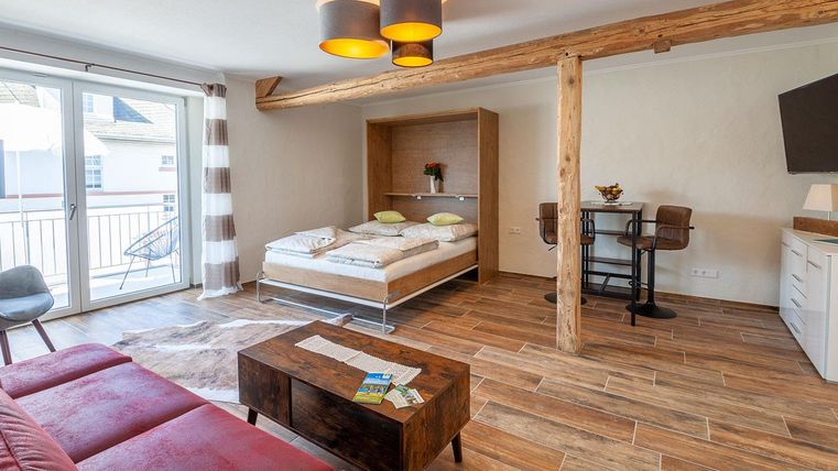 Ein modernes Zimmer mit einem bett, einem Schreibtisch und einer Sitzecke. Große Fenster bieten viel Tageslicht.