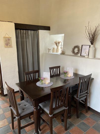 Ein gemütlicher Essbereich mit einem Holztisch und sechs Stühlen. Auf dem Tisch stehen kleine Blumengestecke und Kerzen.