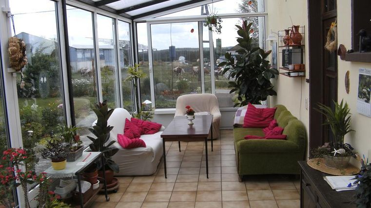 Ein helles Wintergarten mit großen Fenstern und vielen Pflanzen. Gemütliche Sitzgelegenheiten laden zum Entspannen ein.