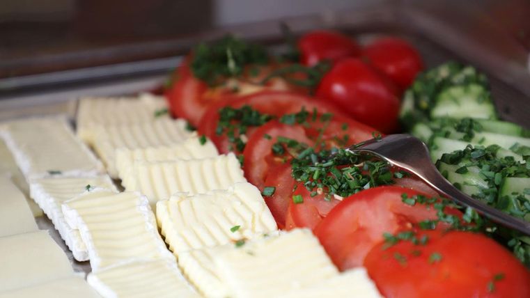 A fresh selection of food with sliced tomatoes, cucumbers, and butter. The ingredients are garnished with fresh chives.
