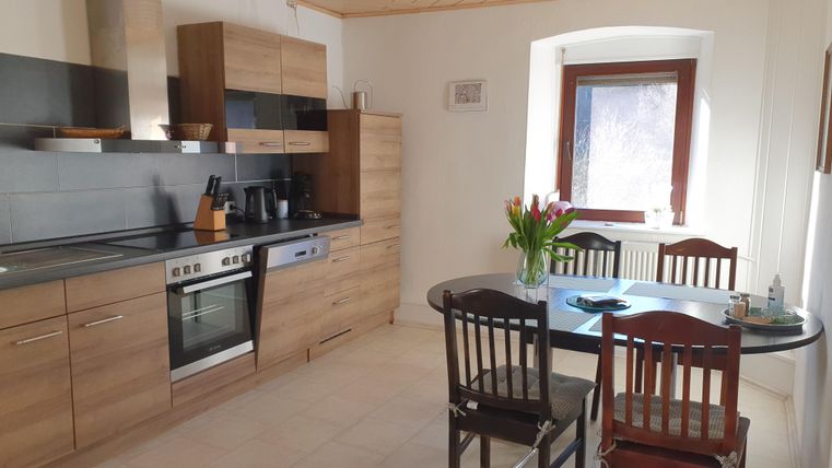 Een moderne keuken met houten kasten en een eettafel. Op de tafel staat een vaas met verse tulpen.