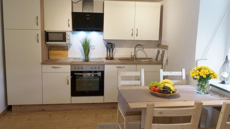 Eine moderne Küche mit weißen Schränken und Holzboden. Ein Esstisch mit Obst und Blumen ist ebenfalls zu sehen.