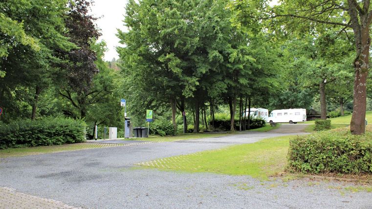 A quiet street surrounded by trees and green spaces. In the background, recreational vehicles can be seen.