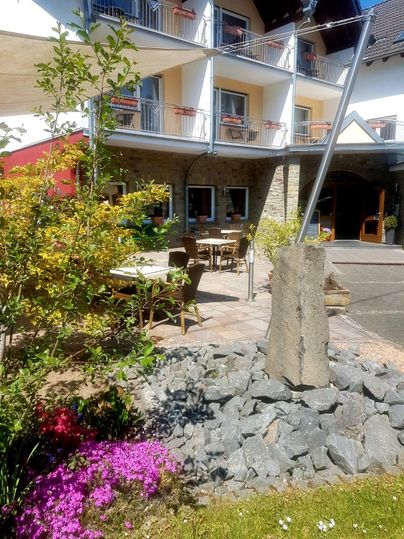 Ein gemütlicher Außenbereich eines Hotels mit Tischen und Stühlen. Bunte Blumen und Steine verleihen der Umgebung einen einladenden Charakter.