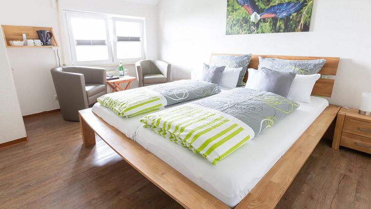 A modern bedroom with a large double bed and colorful pillows. In the corner, there are two cozy armchairs and a table.