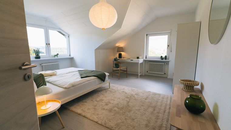 Een slaapkamer met een modern ontwerp en een gezellige sfeer. Er is een bed, een bureau en grote ramen met uitzicht.