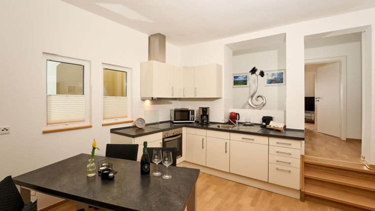 Eine moderne Küche mit einem Esstisch und Stühlen. Die Ausstattung umfasst einen Herd, einen Kühlschrank und verschiedene Küchengeräte.