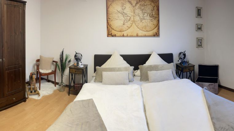 Een gezellig slaapkamer met twee bedden, een grote kast en een raam. De muren zijn eenvoudig, en er zijn enkele planten en decoratieve elementen in de kamer.