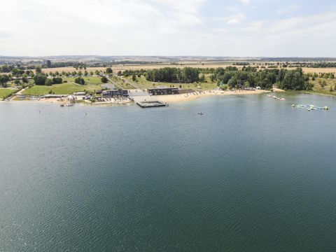 Ein ruhiger See mit einer schönen Strandpromenade. Im Hintergrund sind grüne Wiesen und Bäume zu sehen.