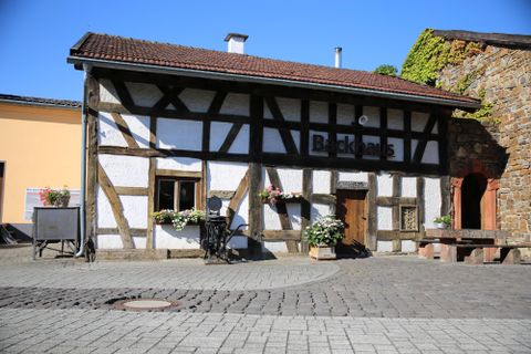 Een klein vakwerkhuis op een grote hof. Boven de voordeur staat de tekst "Backhaus".