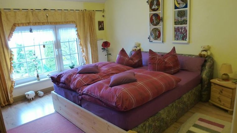 Ein gemütliches Schlafzimmer mit einem großen Bett und bunten Kissen. Das Fenster lässt viel Tageslicht herein und sorgt für eine einladende Atmosphäre.