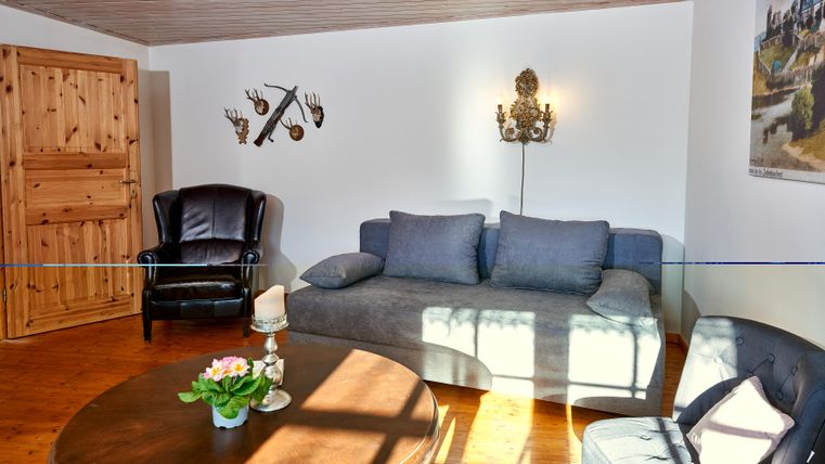 A cozy living room with a blue sofa and a black armchair.
Some decorative elements hang on the wall and the light falls softly on the table.