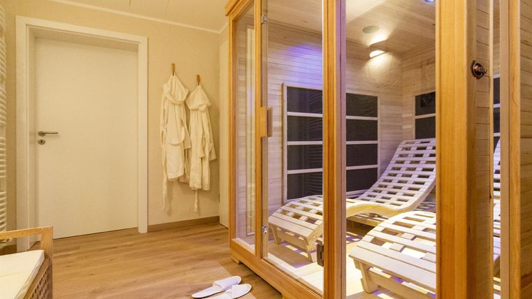 A relaxing area with a sauna and loungers. White bathrobes hang on the wall and the room is brightly lit.