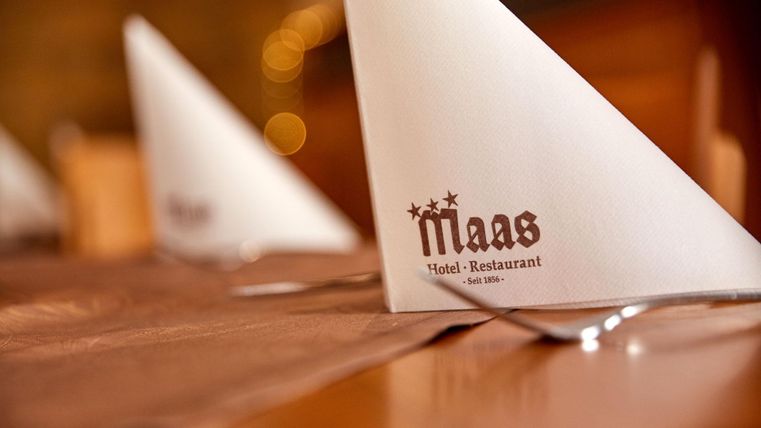 Elegant set tables with folded cloth napkins. The napkins are printed with the name of the restaurant "Maas."