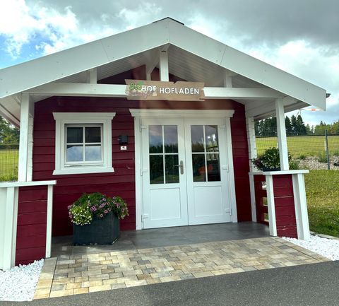 A red wooden house with a white roof and an inviting front door. In front of the house, there are plants in pots, and the area is well-maintained.