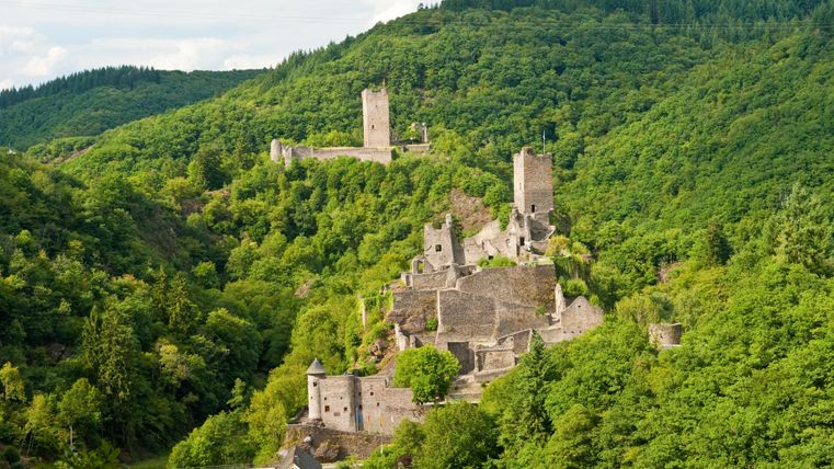 An impressive castle ruin, surrounded by a green landscape. In the background, further tower remnants are visible.
