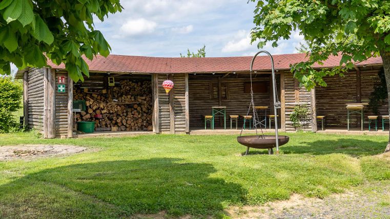 Een gezellige houten hut met gestapeld brandhout. De tuin is groen en uitnodigend, met een schommelstoel en een vuurkorf.