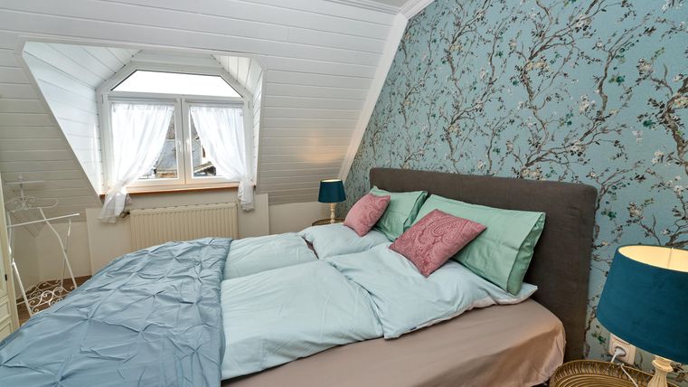 A cozy bedroom with a large bed and fresh bedding in soft colors.
A beautiful floral wallpaper pattern can be seen on the walls, and the window lets in plenty of light.